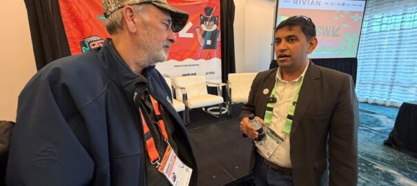 Anurag is in conversation with an event attendee at a conference, discussing sustainable AI and data center impacts, with stage setup and presentation screens visible in the background.